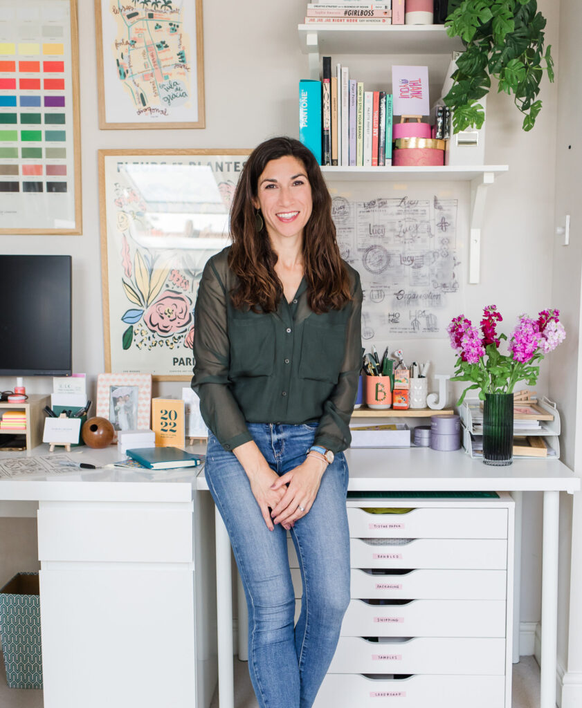 Jen from March and Bloom sitting on the edge of her desk in her branding and graphic design studio