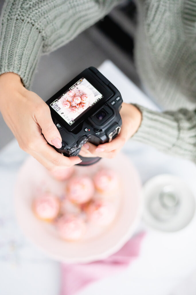 Jessie Bakes Cakes hands holding a camera above some pink cupcakes