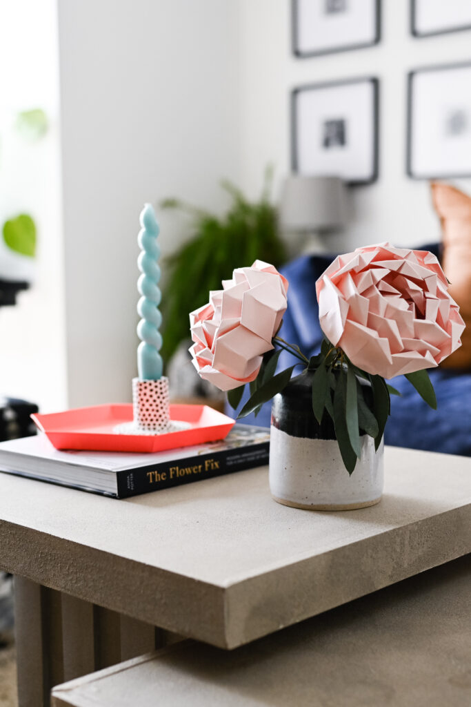Origami Peonies from a Kit by Origami Est, sat in a vase on a table with a candle and book