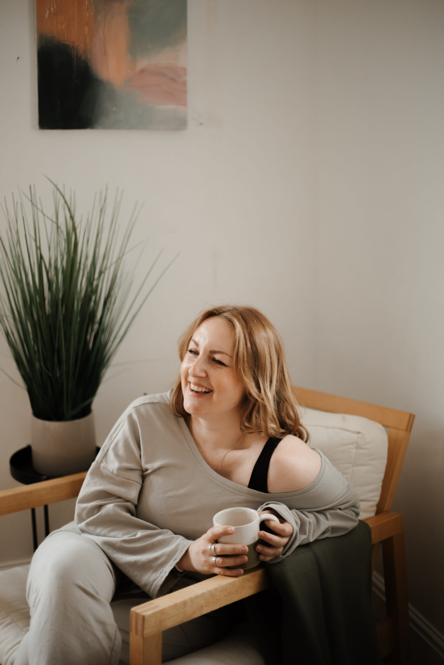 Beth Elsdon Abstract Artist, sitting on a chair with a cup of tea, laughing