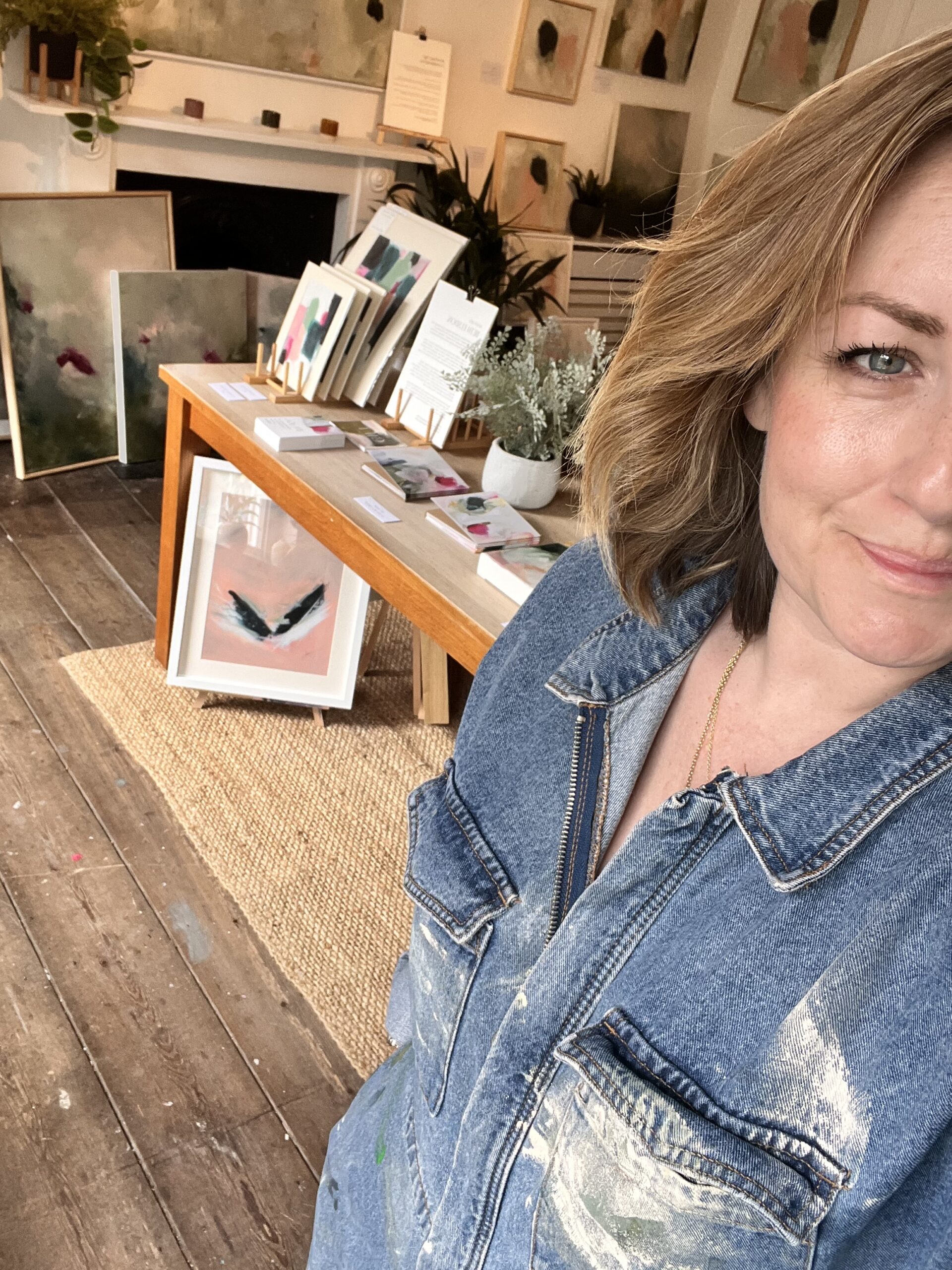 Beth Elsdon in her art studio with art behind her on a table