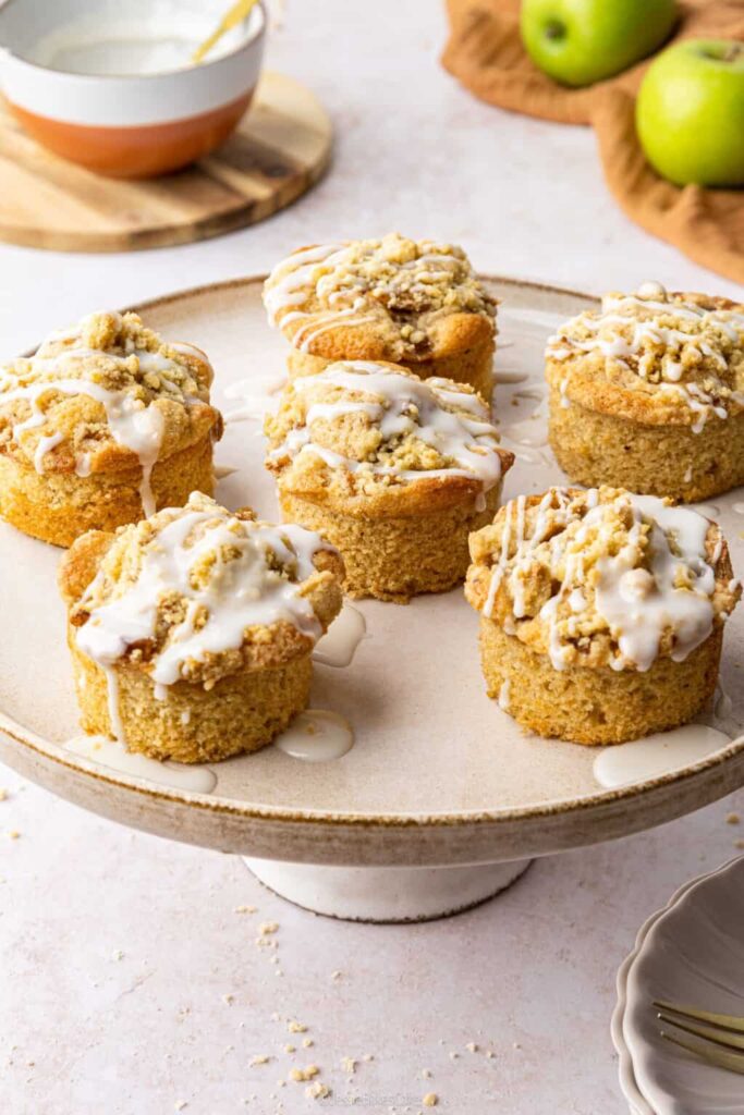 Mini Apple Crumble Cakes on a cake stand with icing drizzled over them, by Jessie Bakes Cakes