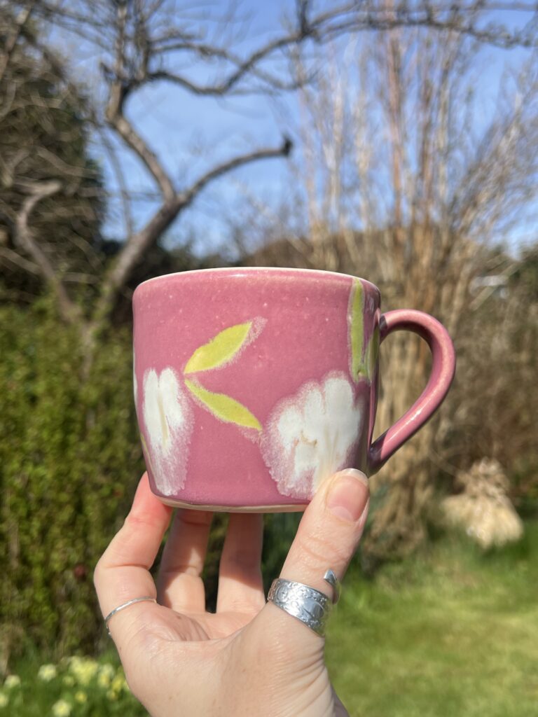 A hand-decorated mug by Ceramics by Kat. Pink with abstract white flowers.