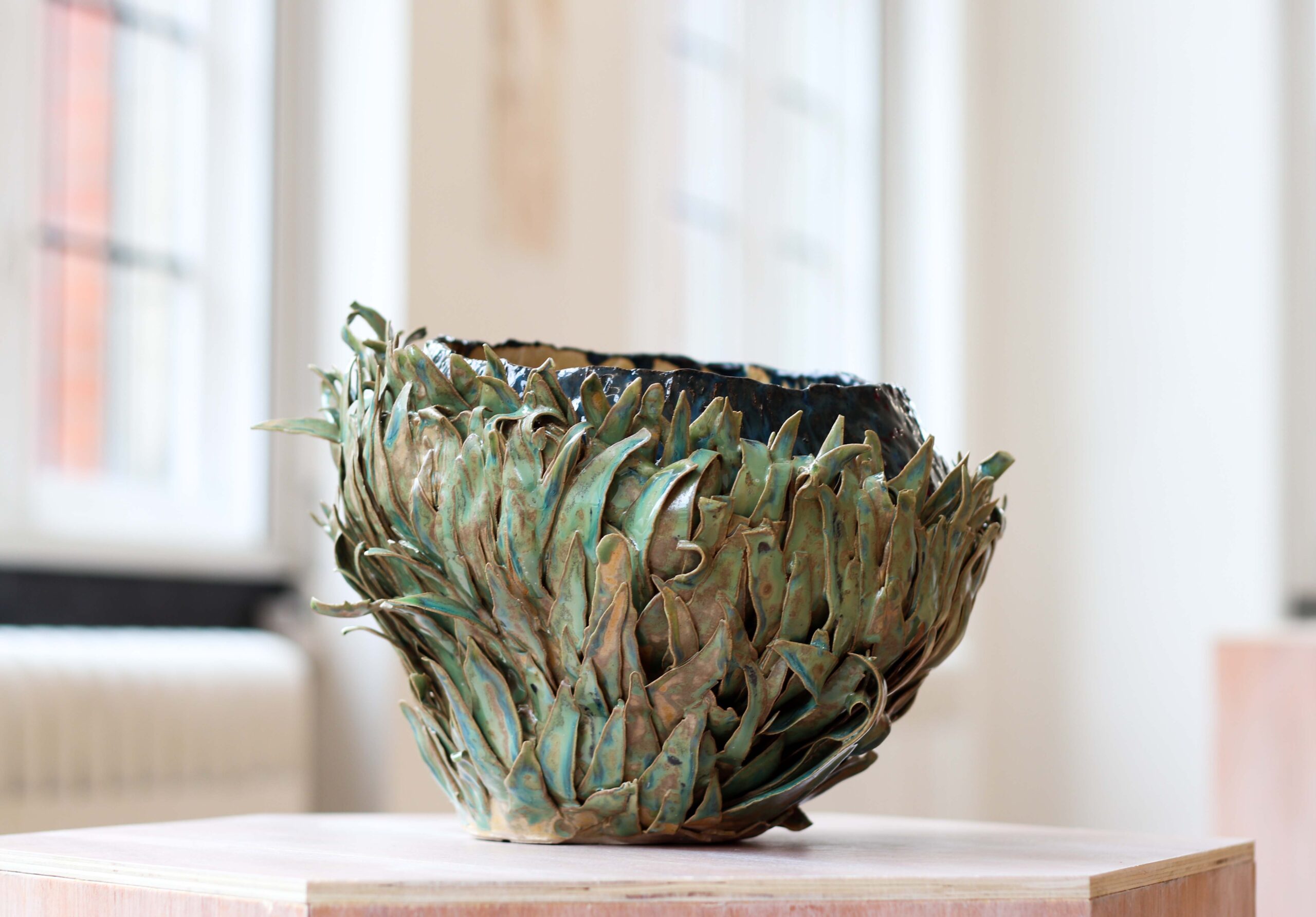 A sculptural piece of clay art by Kat from Ceramics by Kat, created during her time at university. A bowl like structure with layers of long leaves covering the outside - quite organic and natural in form, like a fruit husk or a seed head.