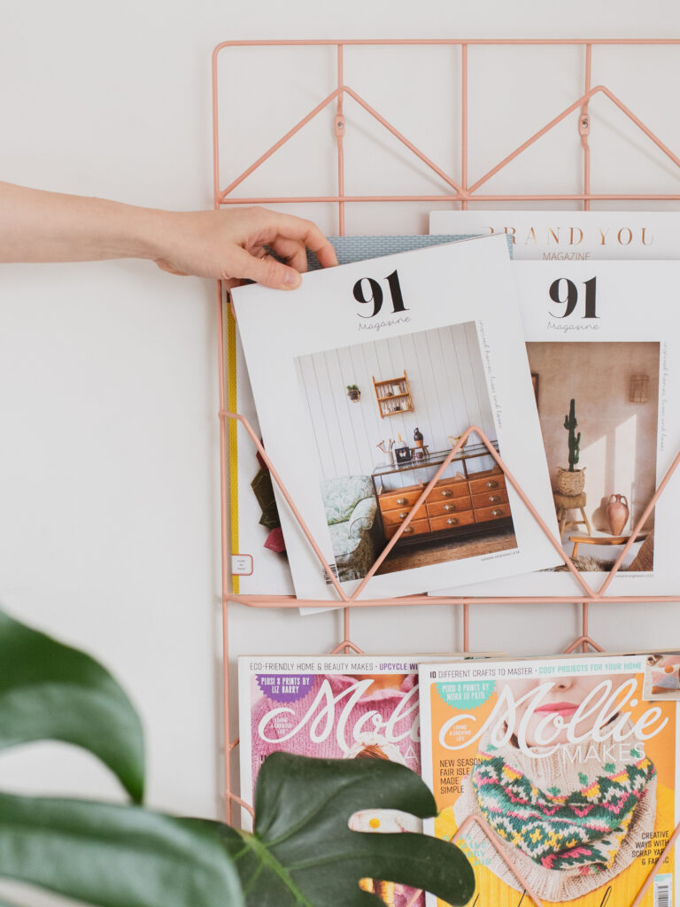 A photo by Holly Booth Studio, showing 91 magazine and Mollie Makes magazine in a gold stand, with a hand reaching for one