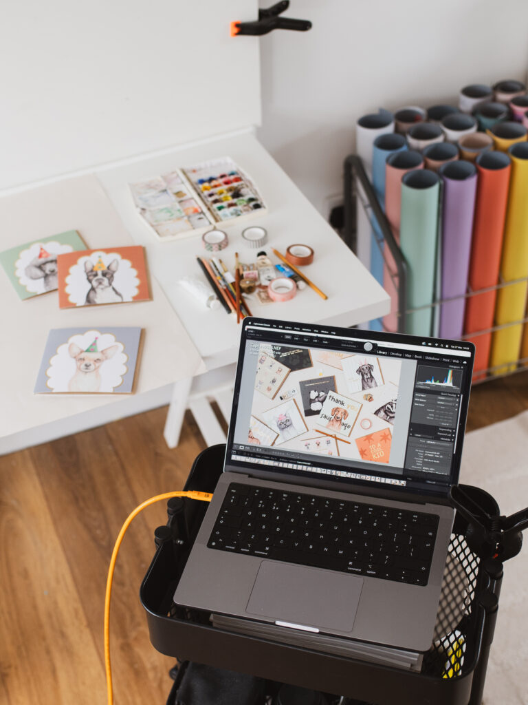 Behind the scenes of Holly Booth Studio's brand and product photography, with a laptop showing the photo just taken and creative items on the table behind