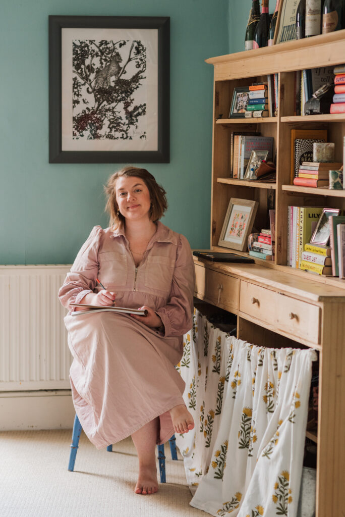 Sarah from Thread The Word, sat sketching, next to a wooden dresser