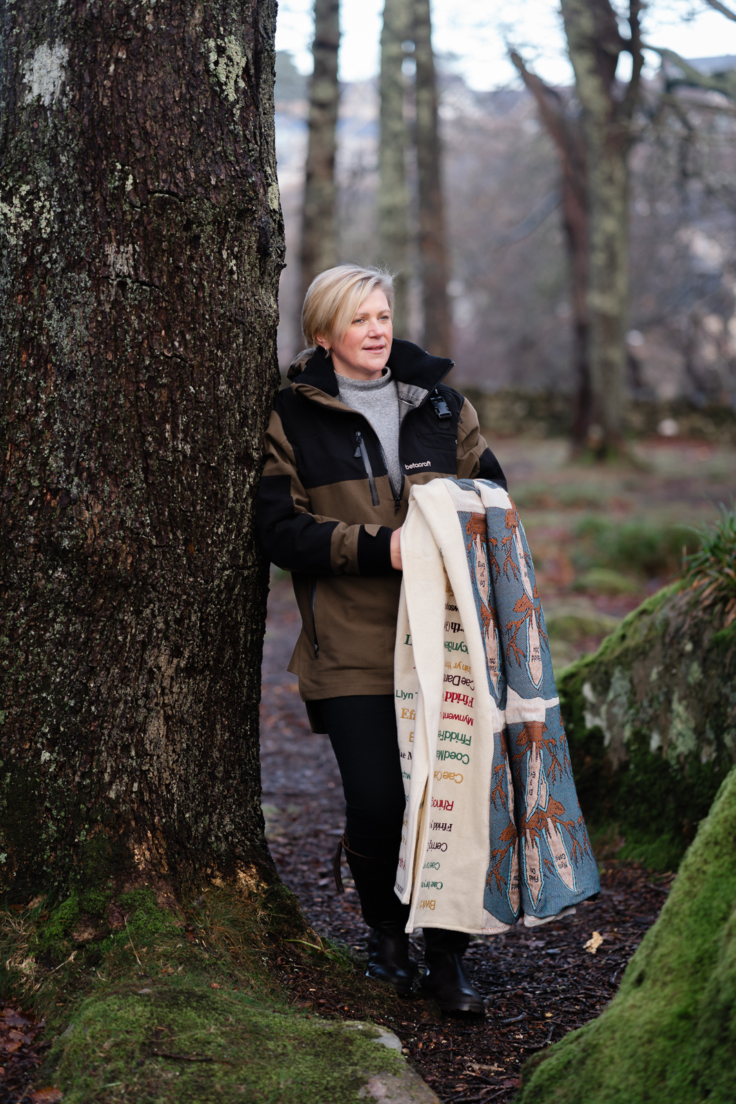 Anna Pritchard textile designer, leaning on a tree, holding one of her textile pieces