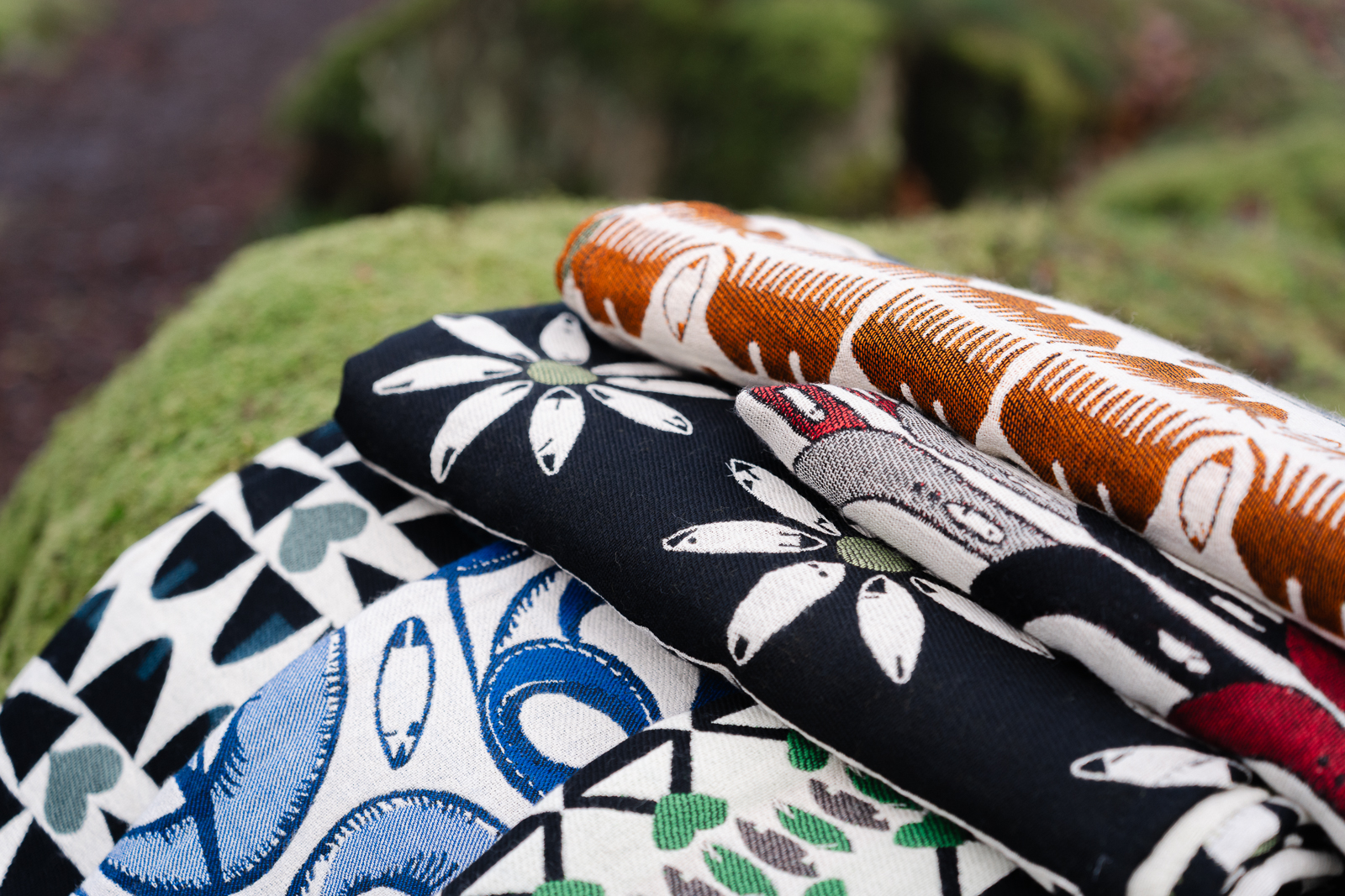 Some blankets by textile designer, Anna Pritchard, folded and stacked on mossy stone.