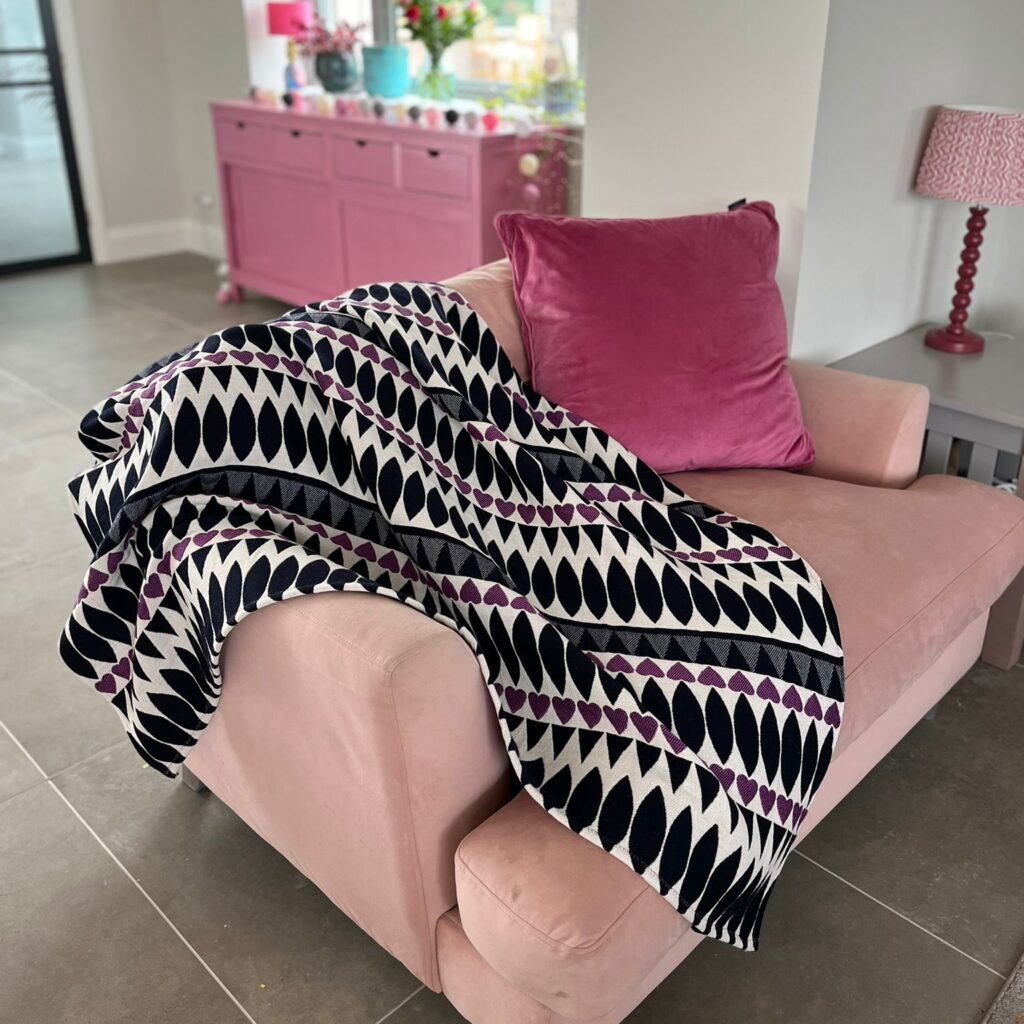 A blanket by Anna Pritchard, draped over a pink sofa with a pink cushion