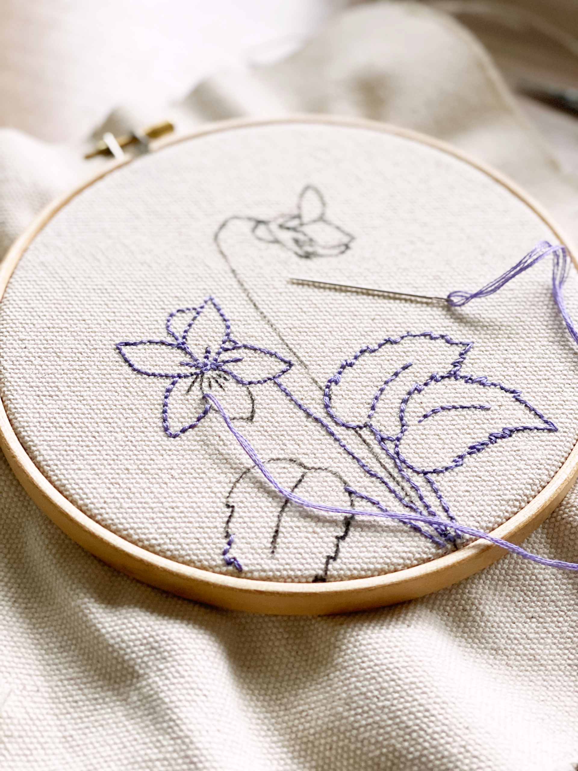 For Creatives' Sake February Birth Flower Embroidery Template project mid stitching, with a wooden hoop, natural cotton canvas fabric, needle, and purple embroidery thread