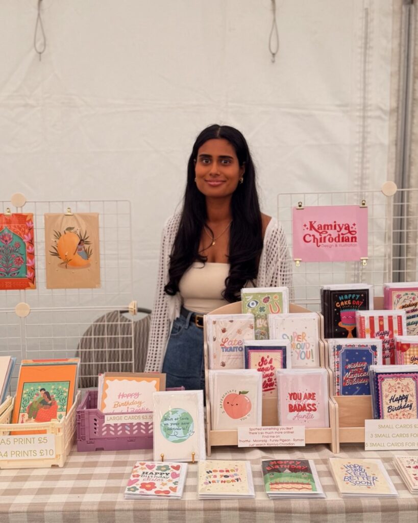 Kamiya Chirodian behind her stall at a market with her cards and prints around her