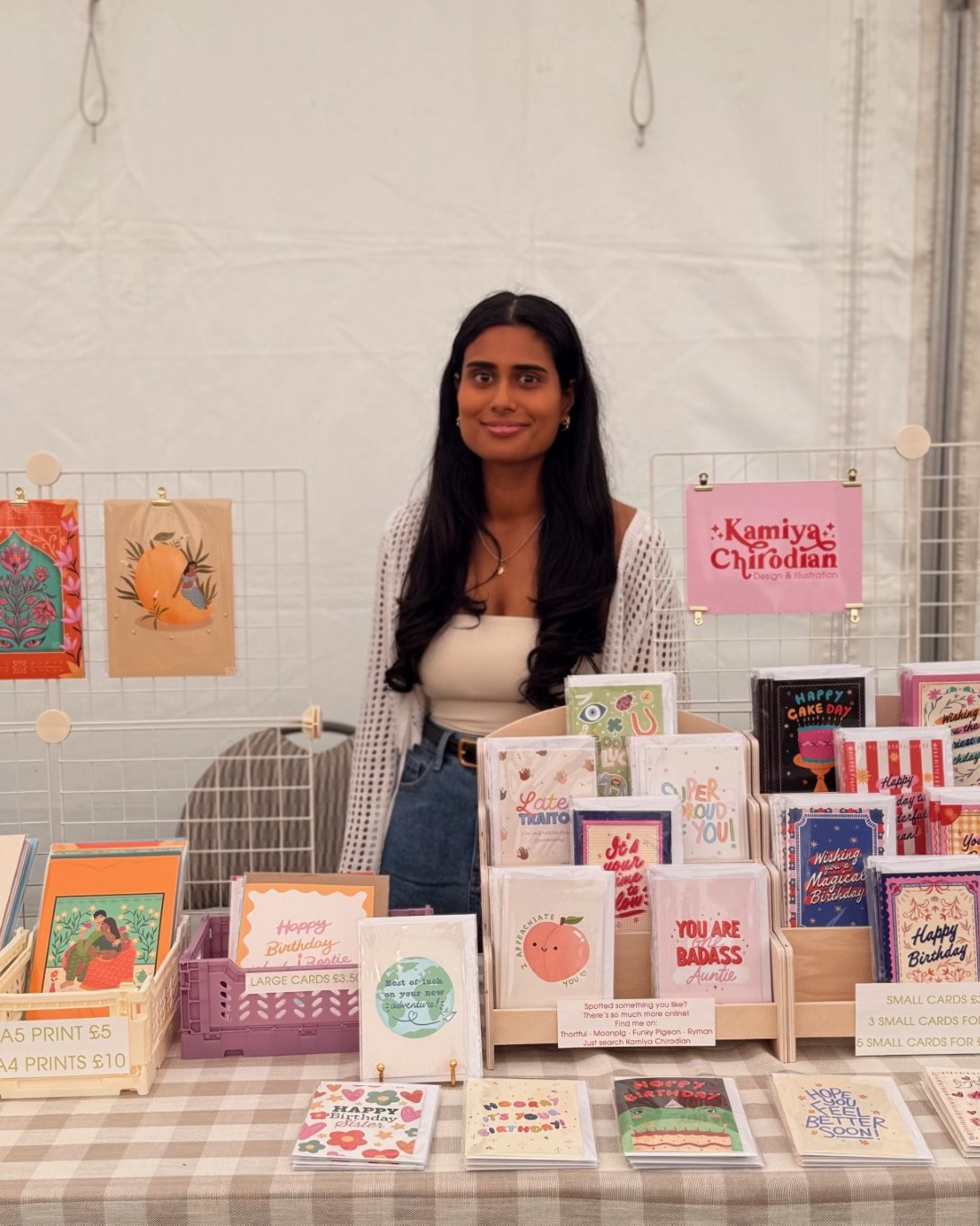 Kamiya Chirodian behind her stall at a market with her cards and prints around her