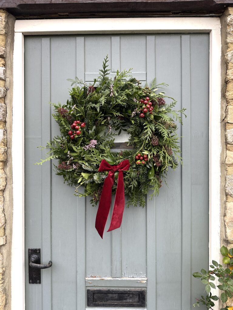 A wreath by Tracey from Wild Soul Flowers, with dark reds, on a sage green front door