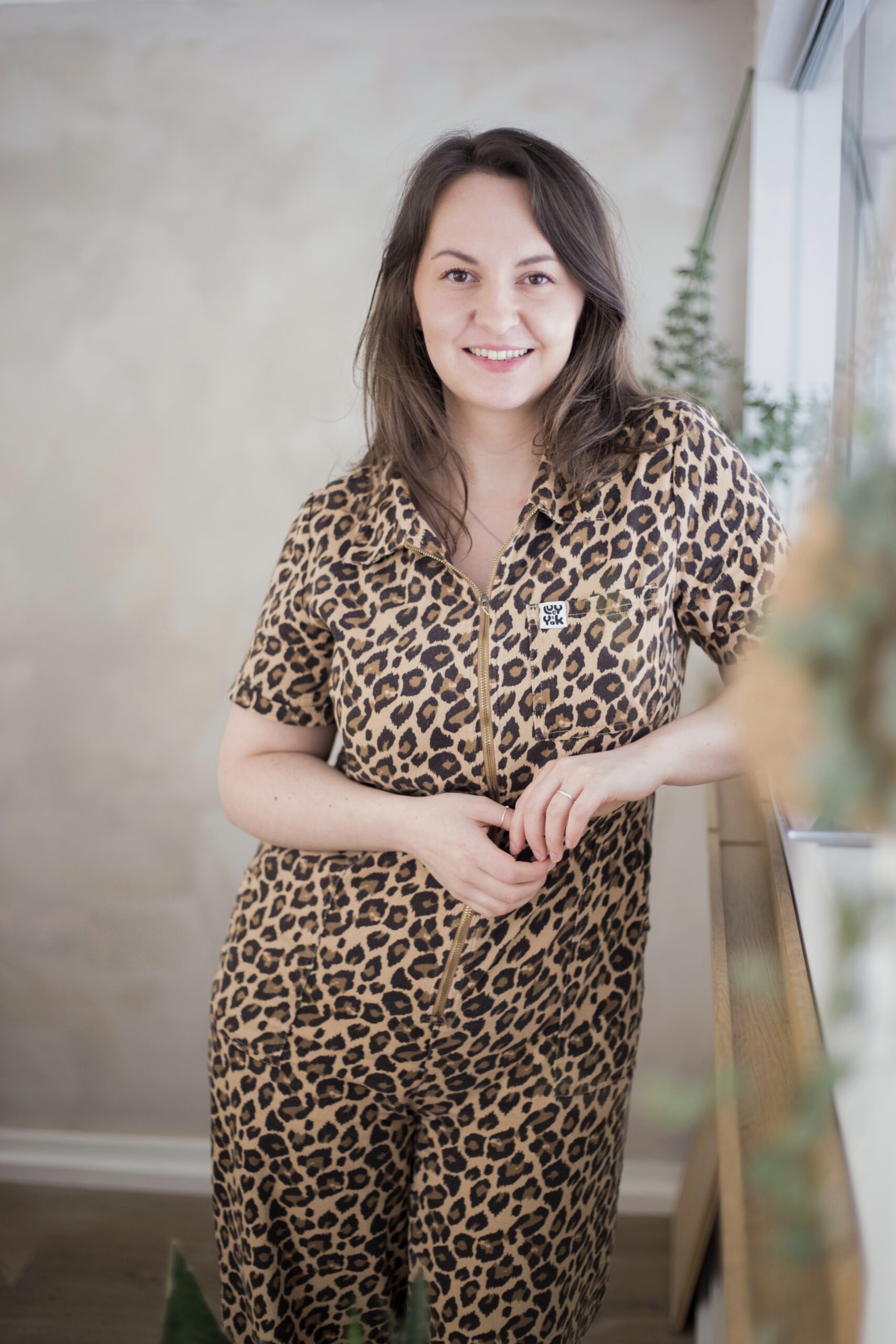 Lucy from Lucy Hannah Photography, leaning on a window ledge in a leopard-print jumpsuit