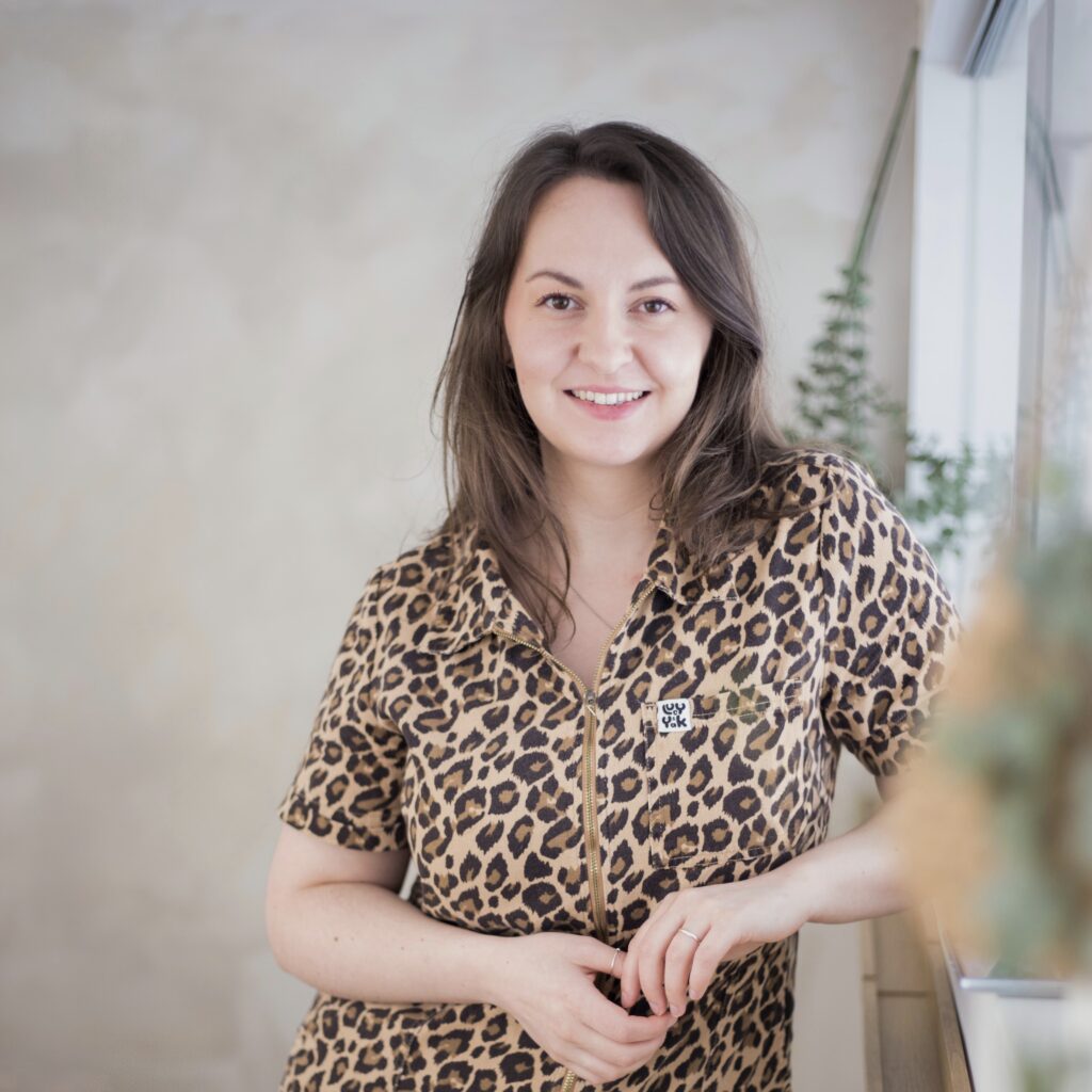 Lucy from Lucy Hannah Photography, leaning on a window ledge in a leopard-print jumpsuit