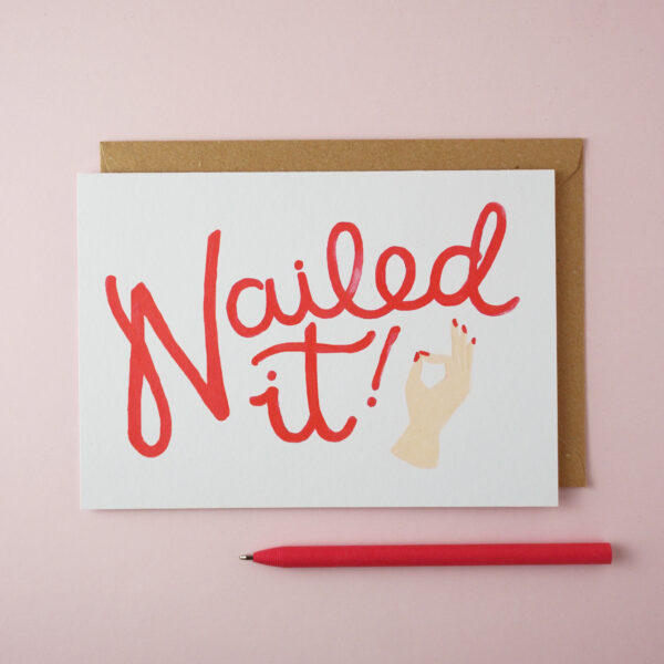 "Nailed it!" card by Jade Fisher, with an illustration of a woman's hand creating the 'okay' gesture and red handwritten style text on the front. A red pen is next to the card. The envelope is brown kraft.
