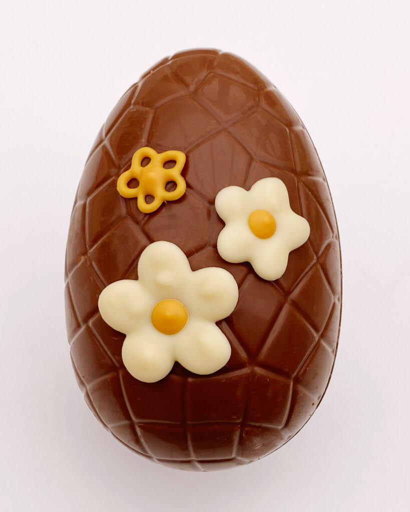 Piped white chocolate flowers on a milk chocolate Easter egg by For Creatives' Sake