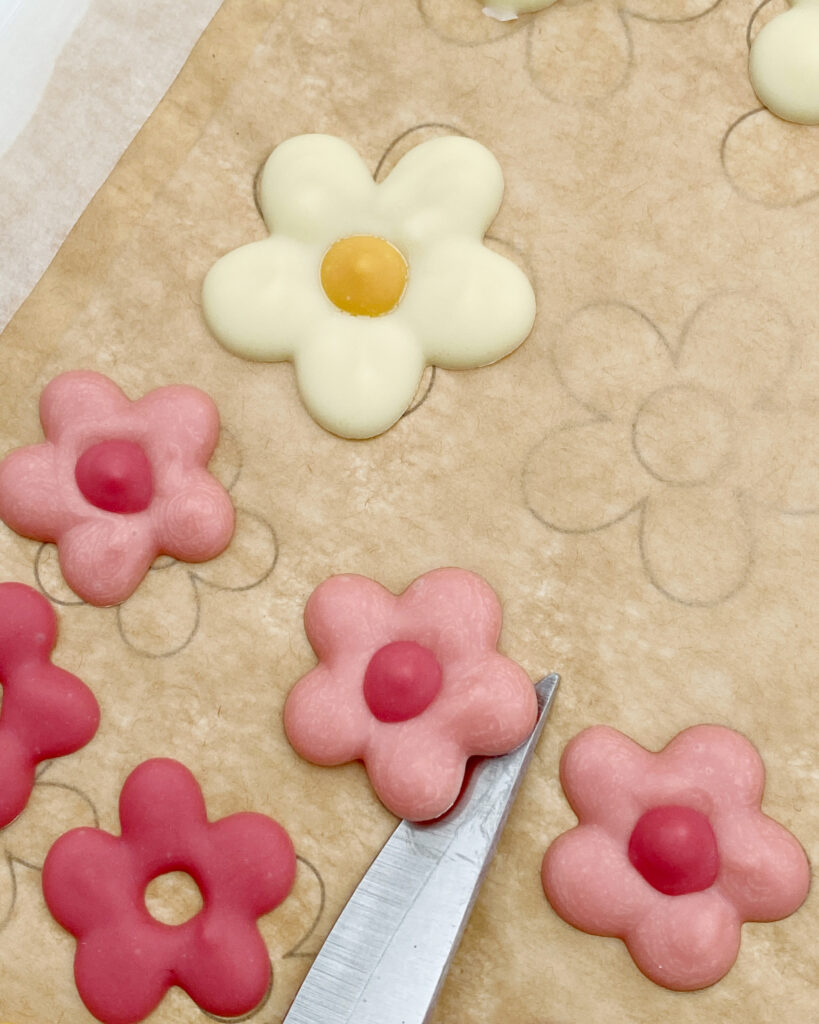 A knife lifting piped chocolate flower transfers off of the non-stick baking paper