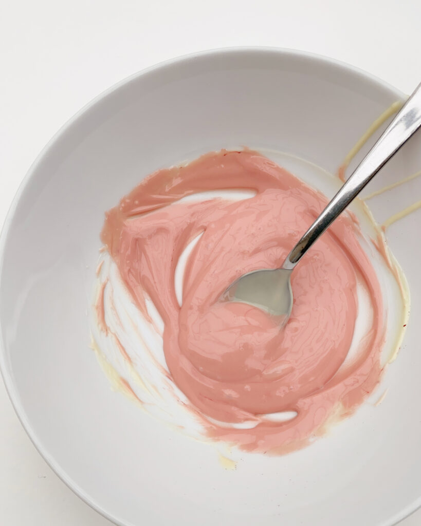 melted white chocolate coloured with some pink food colouring, in a bowl, with a teaspoon