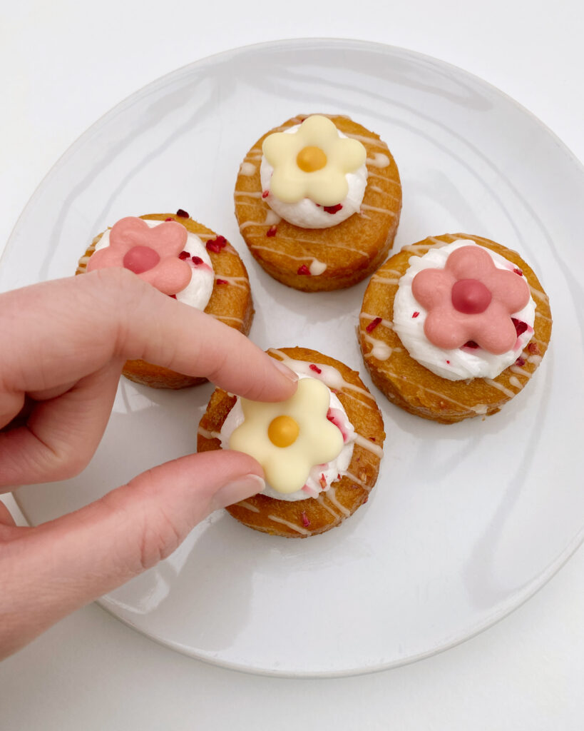 A hand placing a set piped chocolate flower runout onto a mini cake
