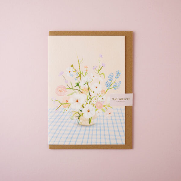 Gingham floral illustrated card by Martha Ratcliff Illustration, with an illustration of a pretty and wild vase of flowers on a blue gingham tablecloth on the front. The envelope is brown kraft.