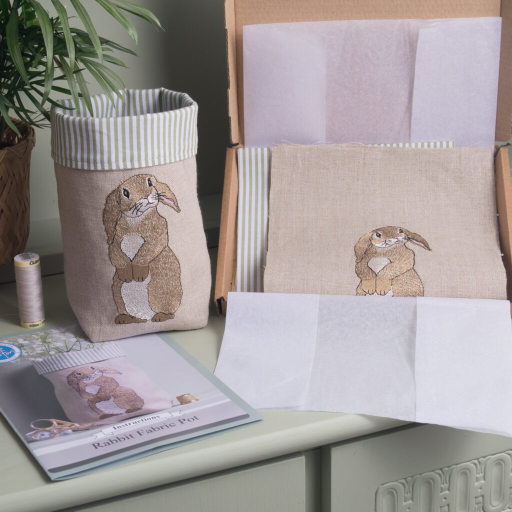 An open box showing a Rabbit Fabric pot kit by Kate Sproston Design, next to a completed fabric pot with an embroidered rabbit on the front