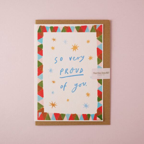 So very proud of you illustrated card by Martha Ratcliff Illustration, with star illustrations and a green, red, and blue patterned border on the front. The envelope is brown kraft.