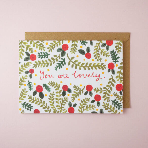 "You are lovely" card by Jade Fisher, with red flower and greenery illustrations, and red handwritten style text, on the front. The envelope is brown kraft.